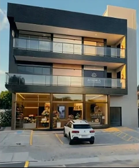 Edifício comercial de três pavimentos com fachada de vidro e acabamento preto, e loja envidraçada no térreo.